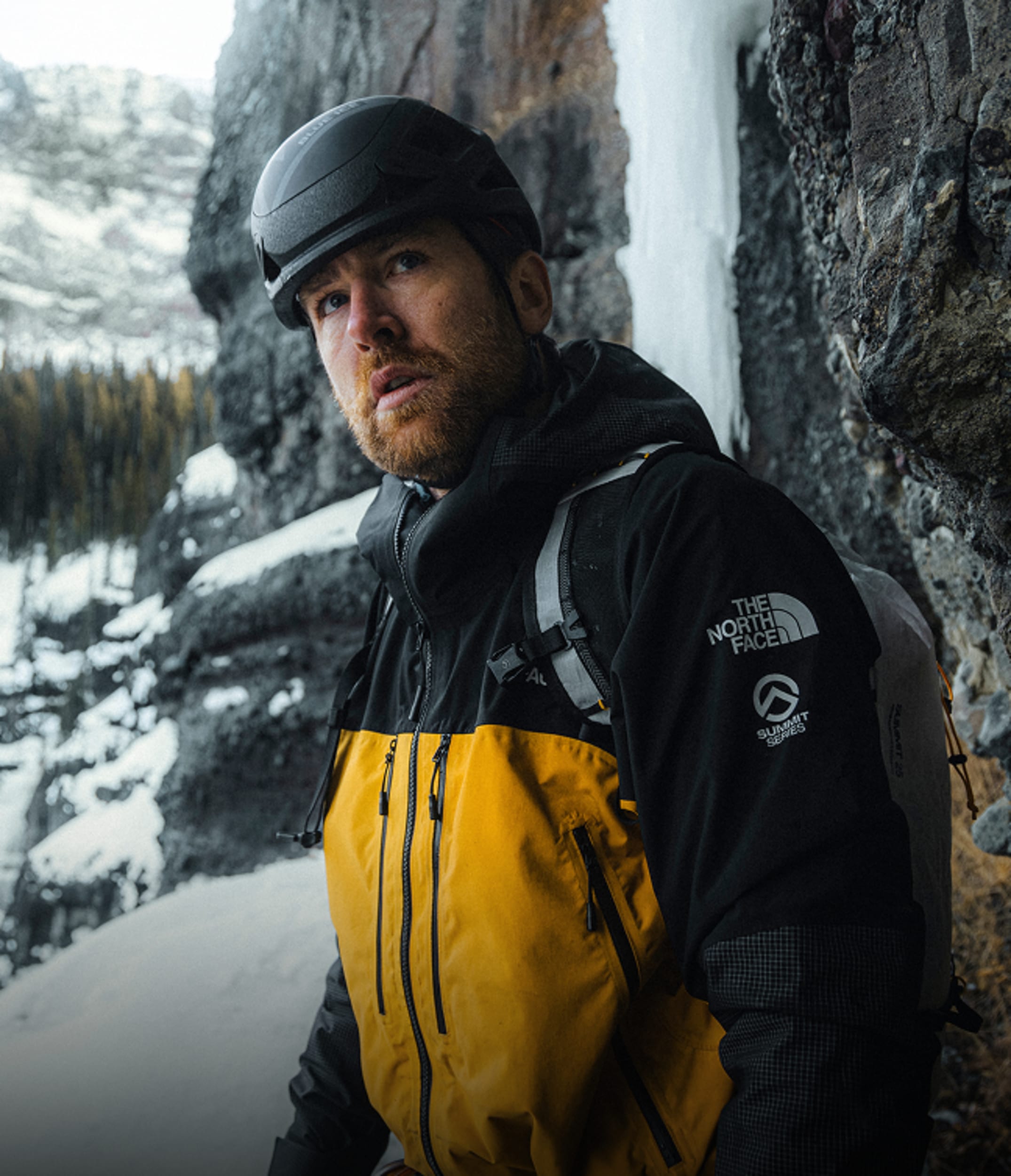 Man in Gold Summit Series Climbing Gear next to a frozen waterfall. 