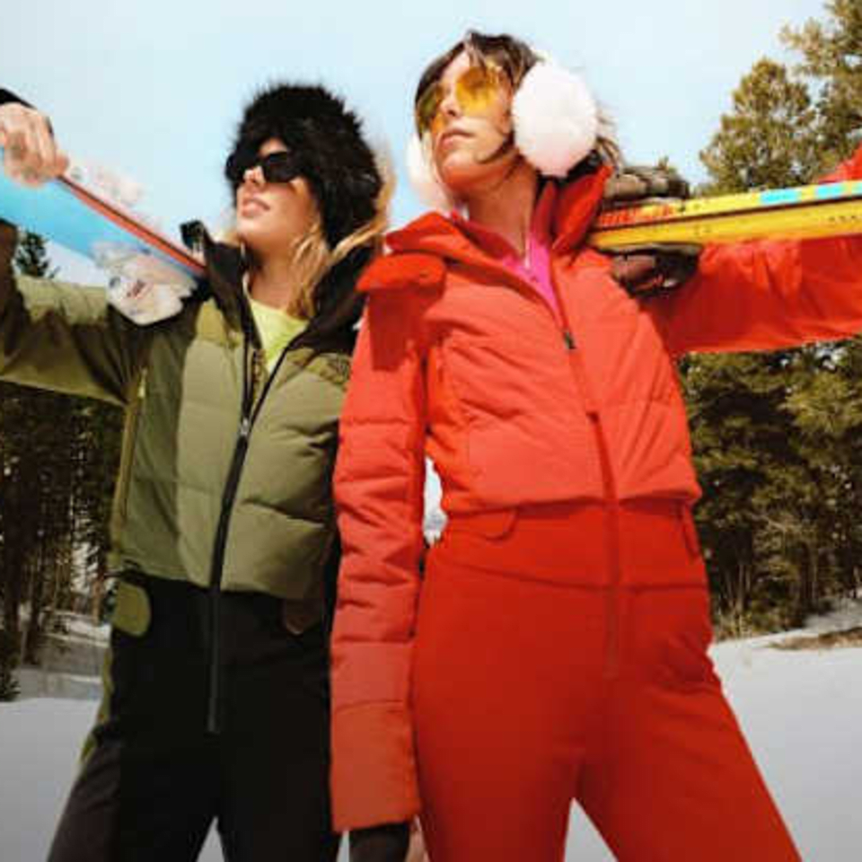 2 girls in snow suits holding skiis on their shoulder in a snowy forest