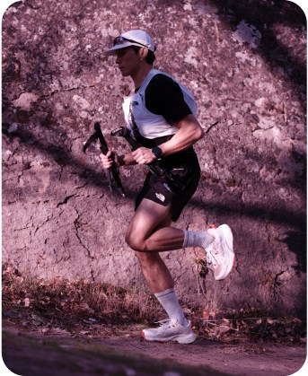 A man running with a white vest and all black attire on a purple backdrop.