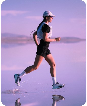 A woman running with a white vest and all black attire on a purple backdrop.