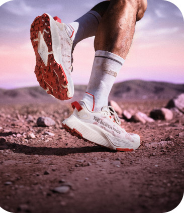 Two legs wearing white Altamesa 500 V2 shoes and The North Face crew socks going for a jog in high-mountain terrain.