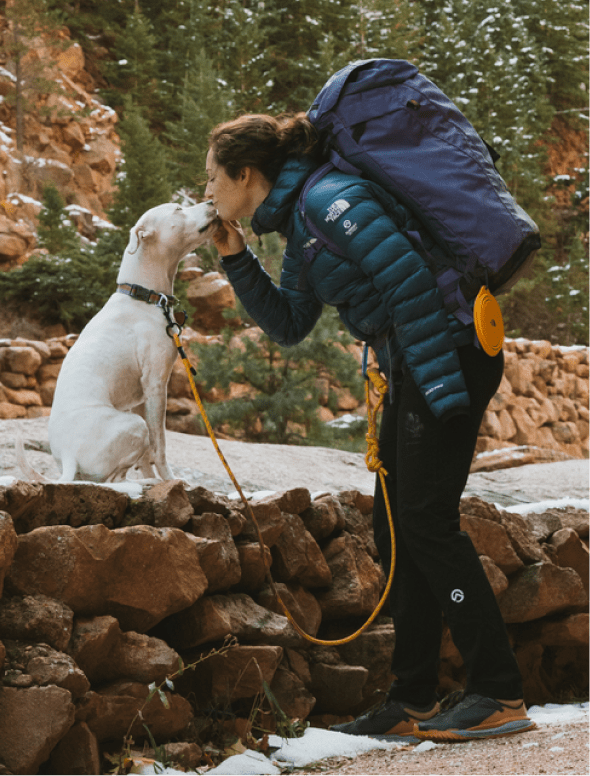 A woman standing nose to nose with her dog in a snowy, rocky landscape while using a The North Face Pet Leash.