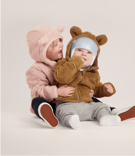 Image of two babies wrapping their arms around one another wearing a fuzzy jacket.