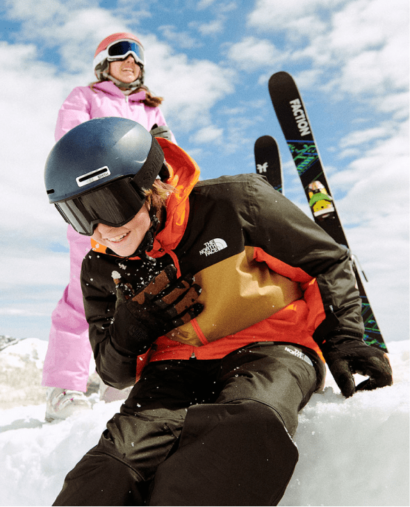 Child bending over with laugher on the mountain surrounded by ski gear.