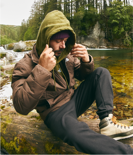 A man in gear from The North Face sits by a stream. 