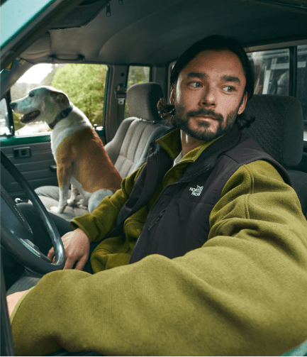 A man in a fleece from The North Face sits in the driver seat of a truck, alongside a dog in the passenger seat.