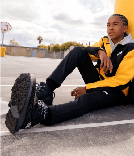 Image of a young boy sitting and the focal point is his The North Face Boots