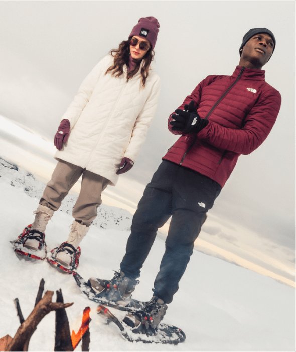 Three people wearing North Face boots strapped to snow shoes in the snow.