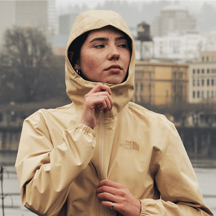 Woman wearing the Daybreak Parka standing in the rain with the city in the background.