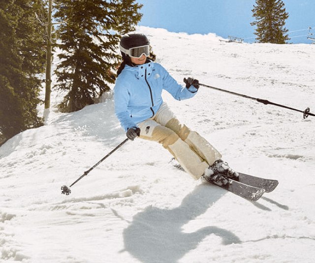 A woman skiing in a light blue jacket and tan pants with a black helmet. 