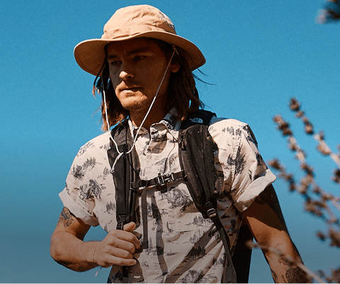 A man hikes in the sun wearing his The North Face hat.