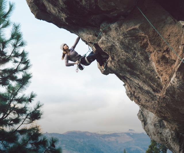 A woman in The North Face gear scales the face of a rock.