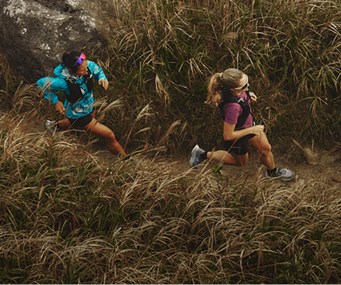 Two women in The North Face gear run through a grassy trail.