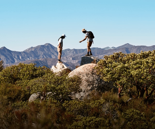 Two hikers rest at a lookout with a panoramic view of the mountains.