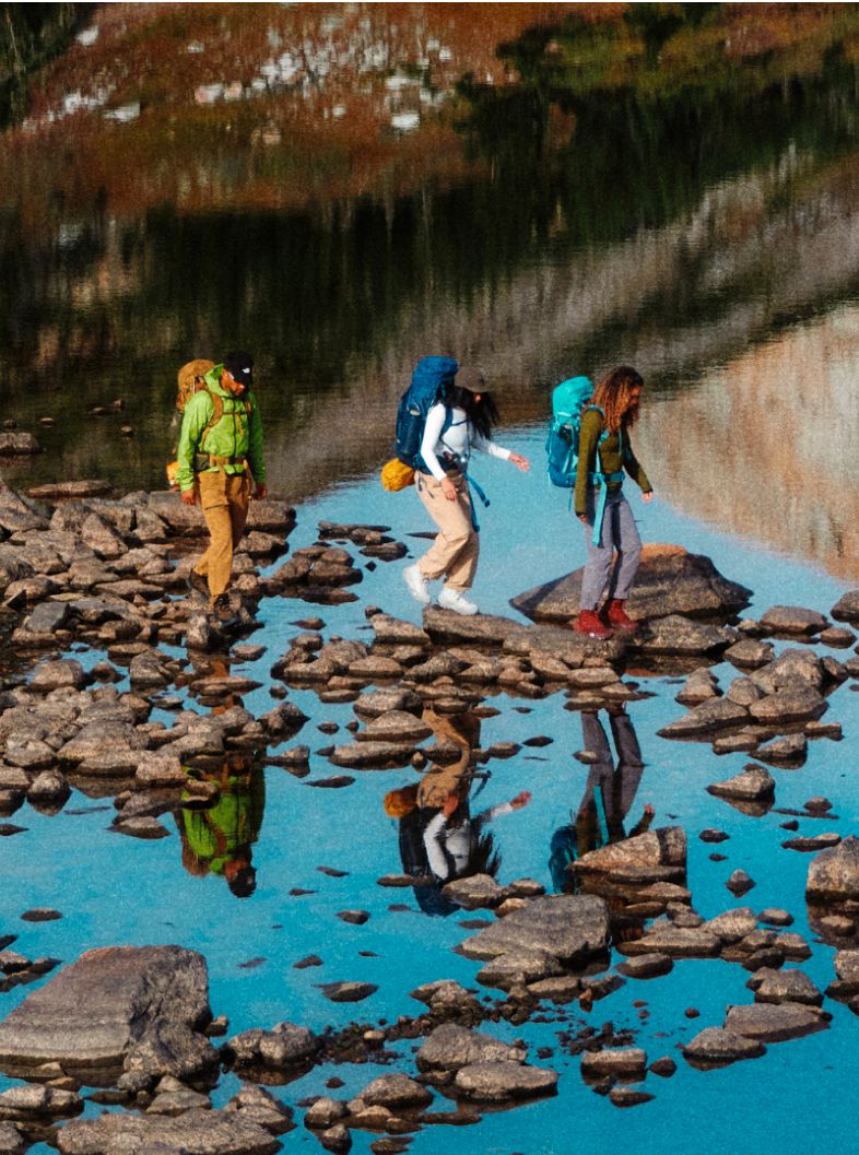 Split image with a photo of red hiking boots sitting atop rocks on the left and a woman in a blue jacket and red boots standing in water to the right.
