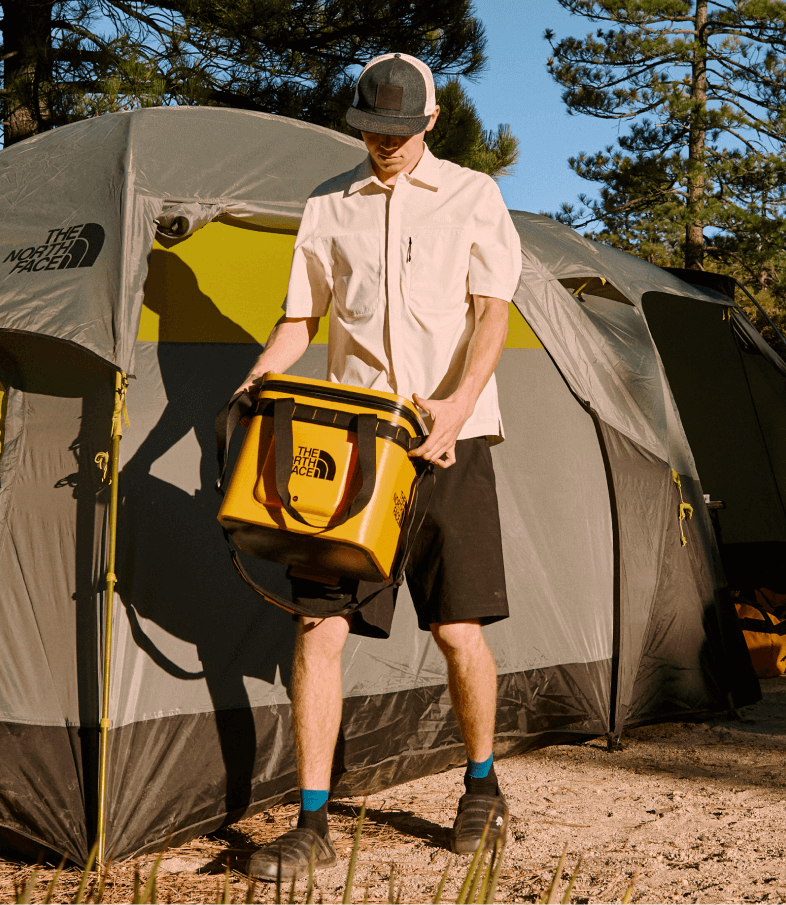 A camper carries the Base Camp Cooler near their tent.