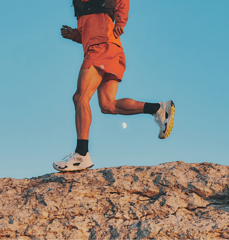 A trail runner runs along a rocky ridge in front of a blue sky.