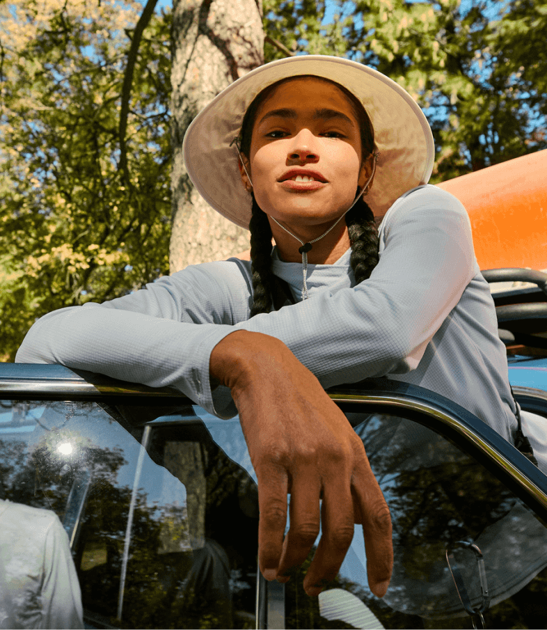 A woman wearing sun-ready gear from The North Face smiles while resting her arms on her car door.