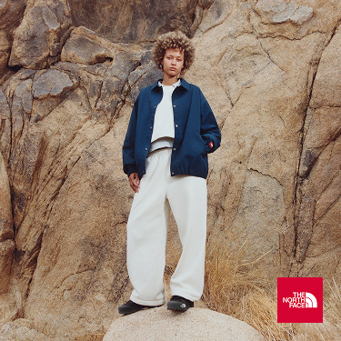 A woman looking at the camera wearing a white shirt and blue jacket. She’s standing in front of rocks.