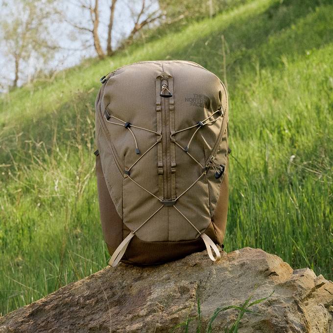 A brown Borealis Trail pack sitting atop a rock with a grassy hill in the background.