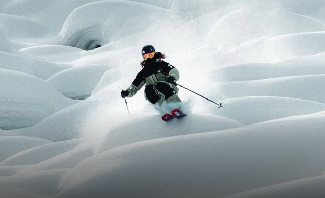 A wide shot of a skiier going down a mountain with a cloud of snow behind them.