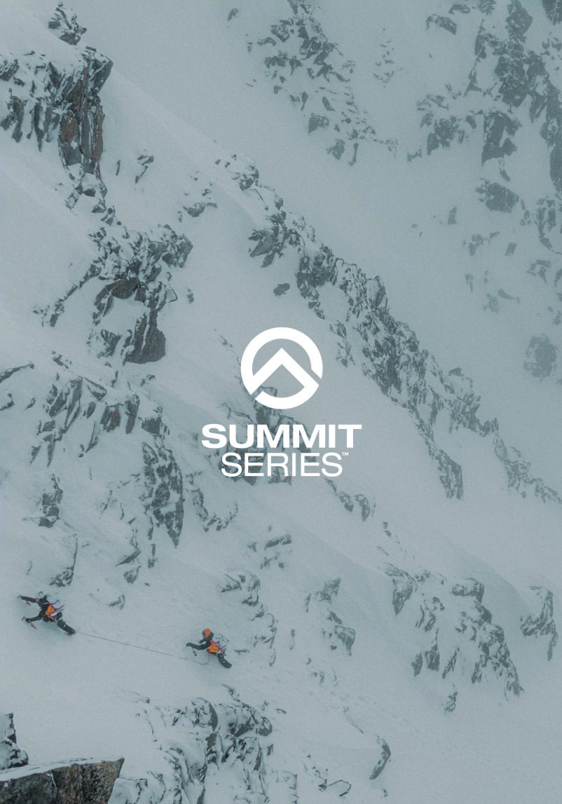 Wide shot of two alpinists tethered by a rope climbing up a snowy rock face.