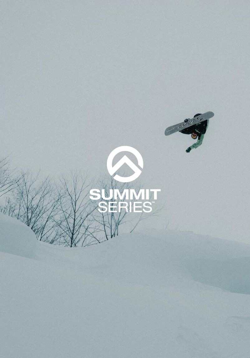 Plan large d'un snowboardeur en plein vol, tenant sa planche d'une main. Il commence à effectuer un salto. La personne est à droite de la photo.