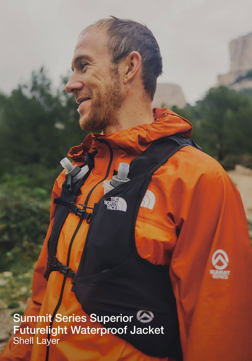 The upper half of Jon’s body. He’s wearing an orange jacket and black running vest while looking to the left.