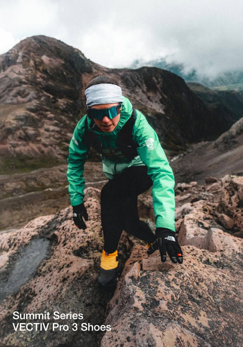Tara moving across rocks wearing a gray headband and turquoise jacket. Her shoes are yellow and black.