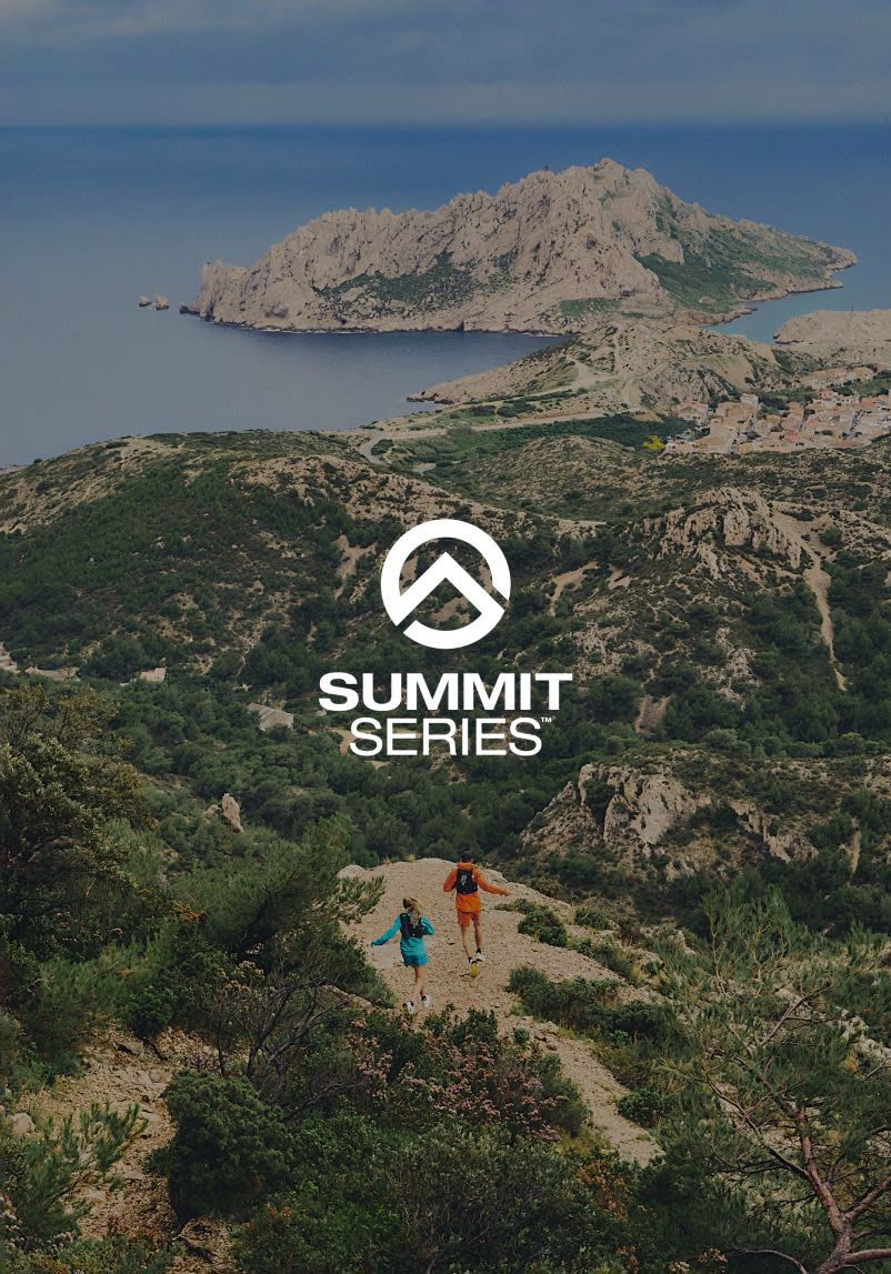 A wide shot of Jon in all-orange and a woman in all-blue running through the hills towards a body of water. 