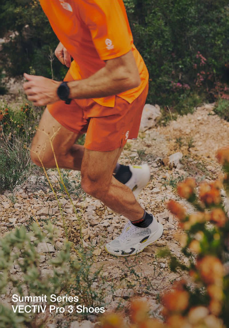 A close up of Jon’s torso and lower body as her runs uphill. He’s in an all-orange outfit with a black watch and no running vest. 