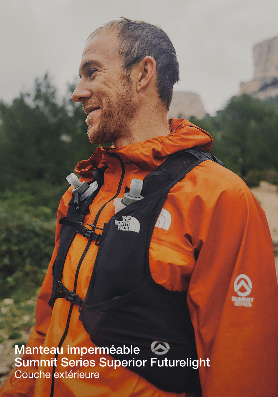 La partie supérieure du corps de Jon. Il porte une veste orange et un gilet de course noir et regarde vers la gauche.