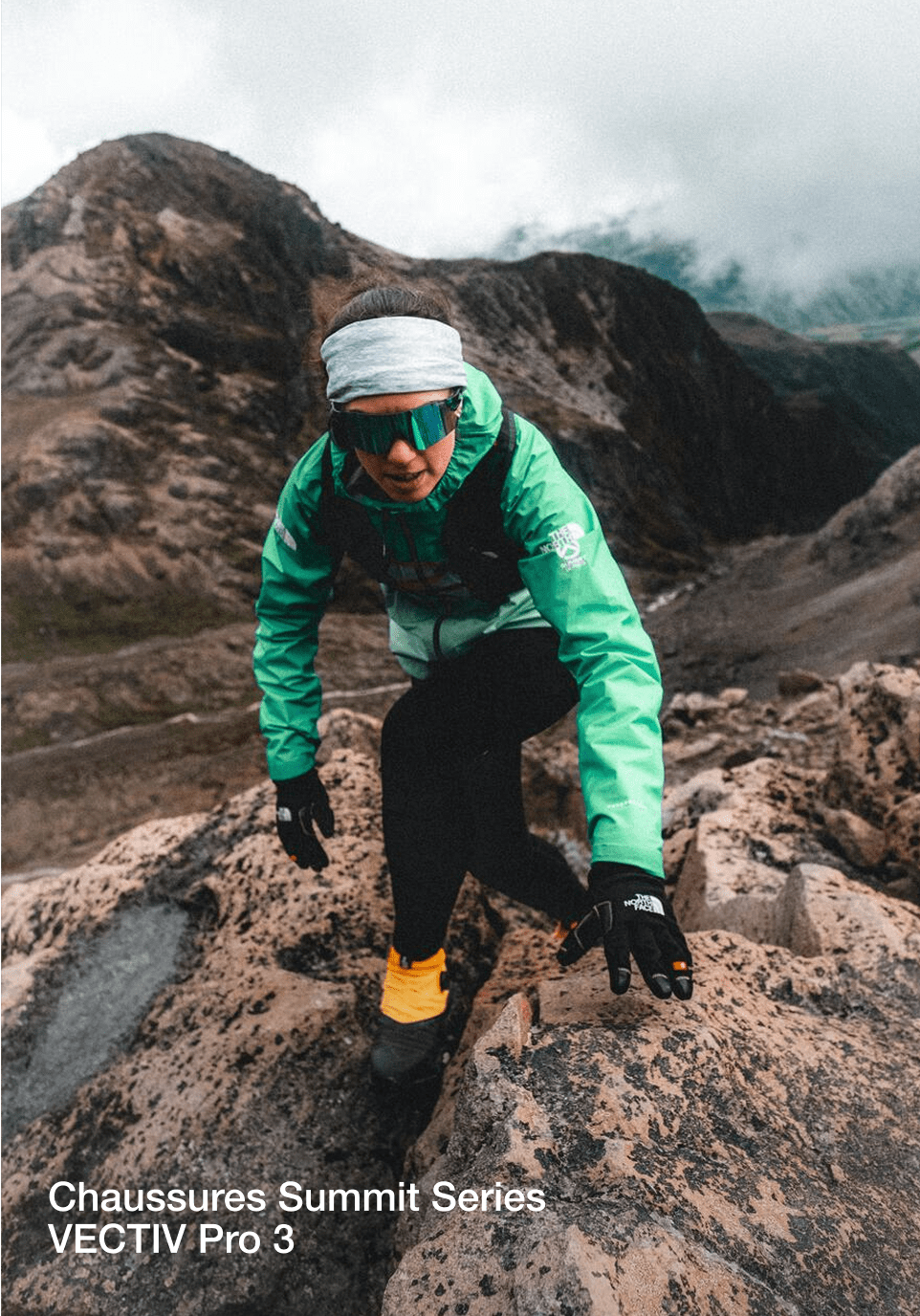Tara se déplace sur les rochers, vêtue d'un bandeau gris et d'une veste turquoise. Ses chaussures sont jaunes et noires.