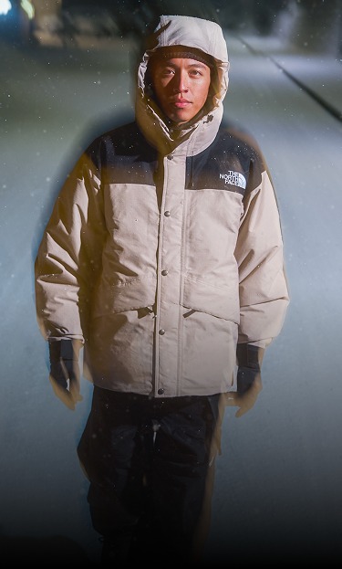 De nuit, un homme marche sur une route enneigée, vêtu du manteau The North Face Mountain Down Jacket en gris champignon.  