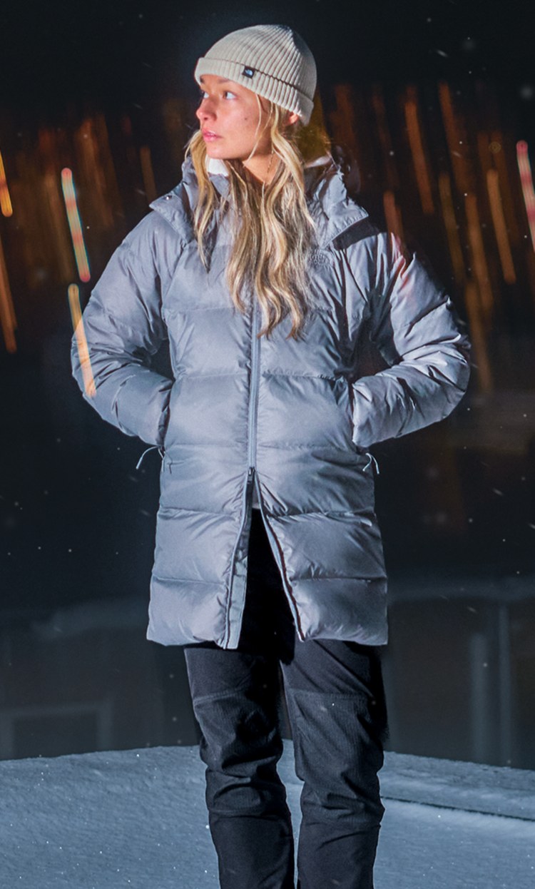 A female stands outdoors under a clear blue sky wearing The North Face Jacket in pearl.
