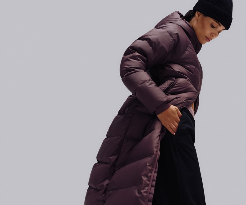 A female stands against a dark gray background wearing The North Face Hydrenalite City Down Hooded Jacket.