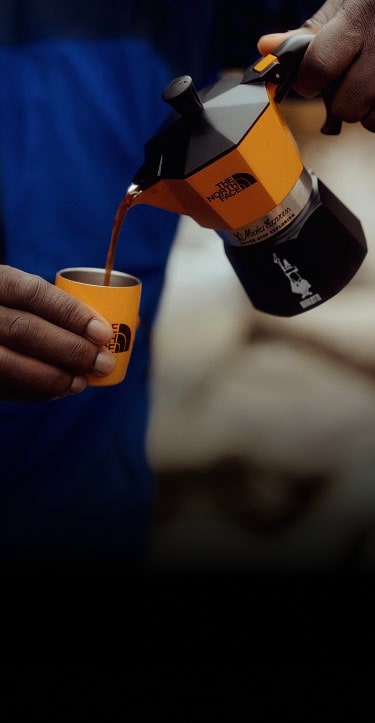 Person in a blue jacket from The North Face pouring coffee.
