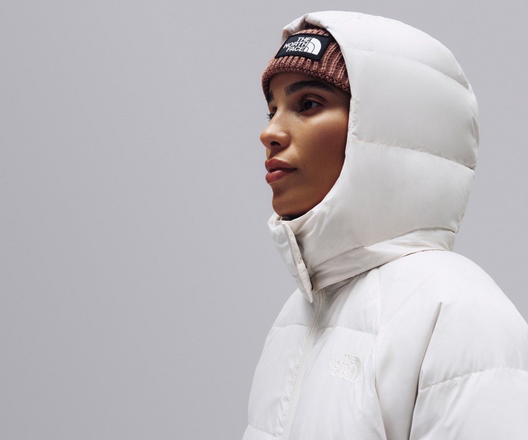A female stands in profile against a light gray background wearing The North Face Hydrenalite City Down Hooded Parka in White.