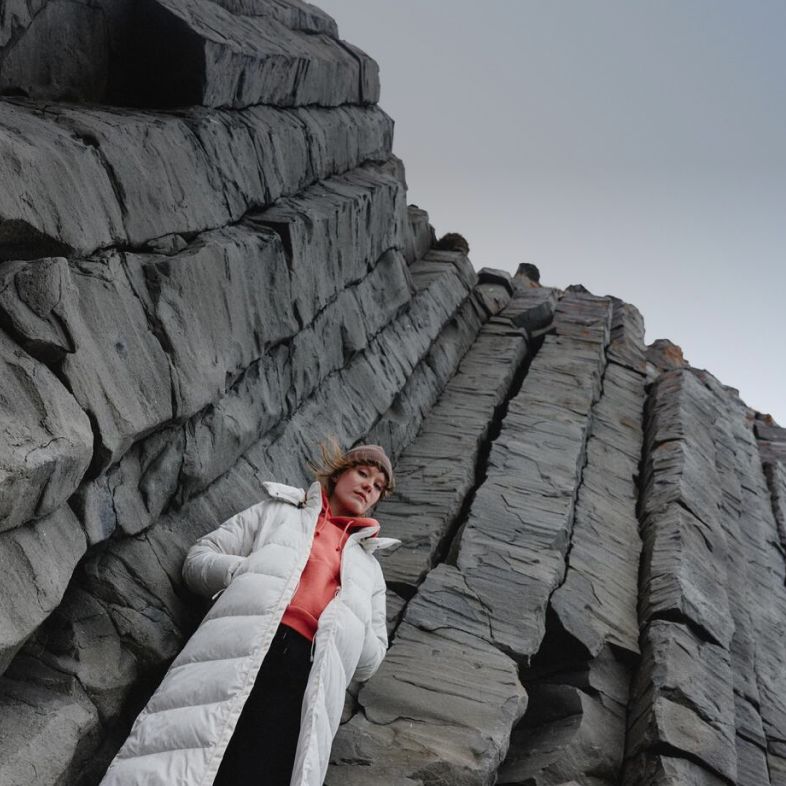 Woman standing in front of a rock wall wearing a white parka from The North Face.