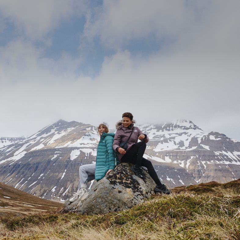 Two women sitting on a rock with a snowy landscape in the background.