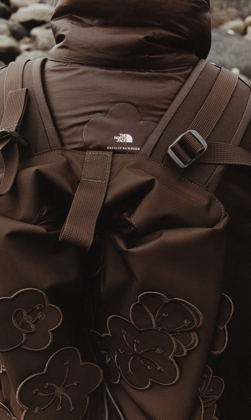 A close-up of someone from behind in a brown puffer and brown, flowery backpack.