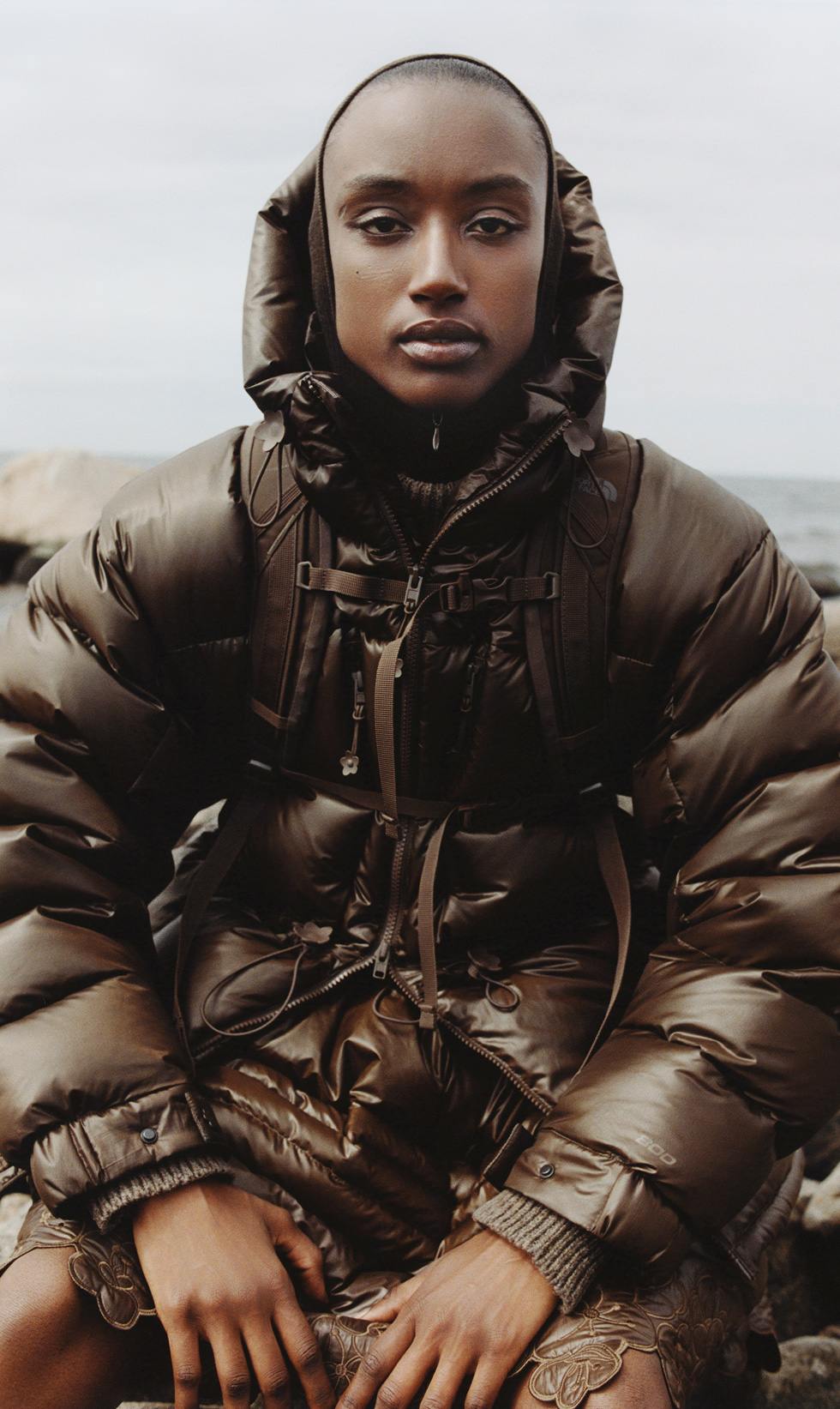 A woman in a brown puffer and a brown backpack looking directly at the camera.