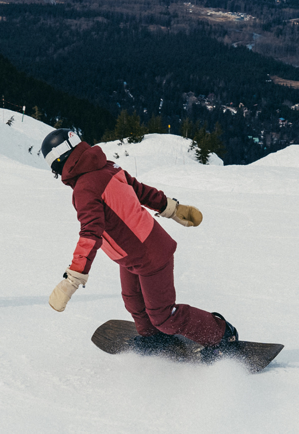 Two snowboarders ride down a snowy mountain, the woman wearing The North Face Women’s THERMOBALL™ Snow Triclimate® Jacket in Sumac/Mars Dust. A third image shows them hiking uphill with their boards in hand, surrounded by fresh powder and mountain views. 