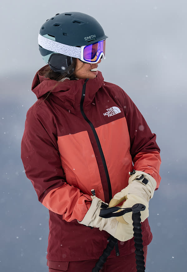 Two snowboarders ride down a snowy mountain, the woman wearing The North Face Women’s THERMOBALL™ Snow Triclimate® Jacket in Sumac/Mars Dust. A third image shows them hiking uphill with their boards in hand, surrounded by fresh powder and mountain views. 