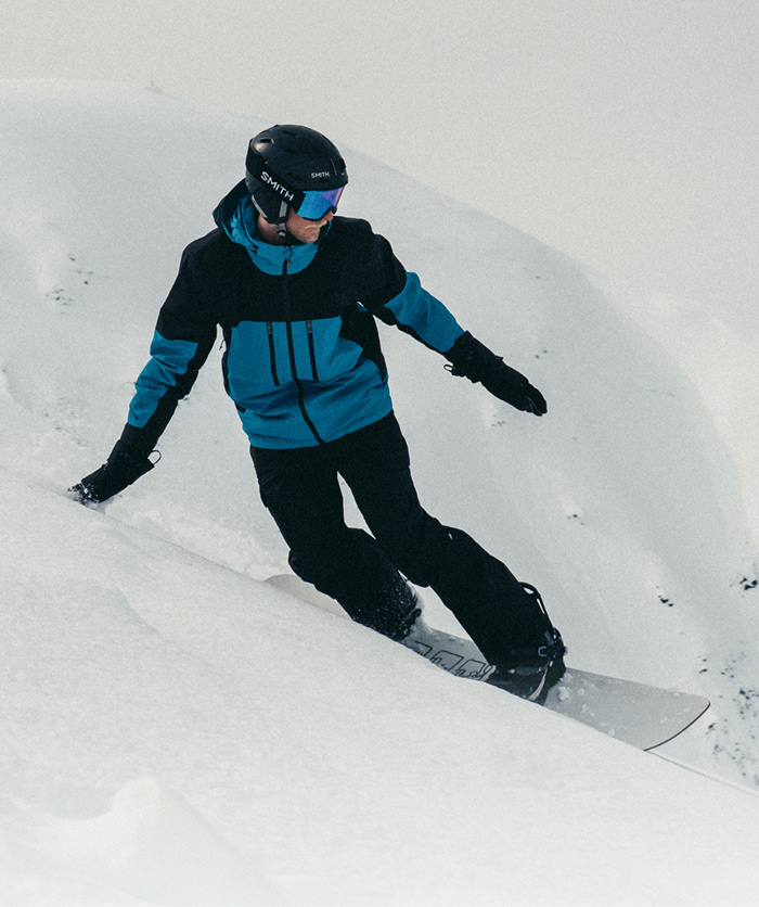 A woman in a white hoodie/white beanie/turquoise jacket with her arms stretched out. 