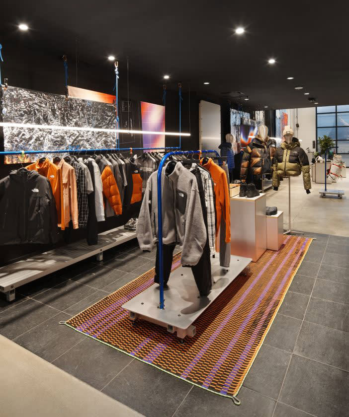 An image of clothes racks in one of our stores. The main rack has a gray fleece, an orange fleece and a flannel hanging.
