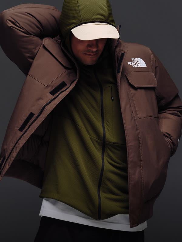 Male model reaching his hand behind his head in McMurdo Bomber in Smokey Brown over a green hoodie.