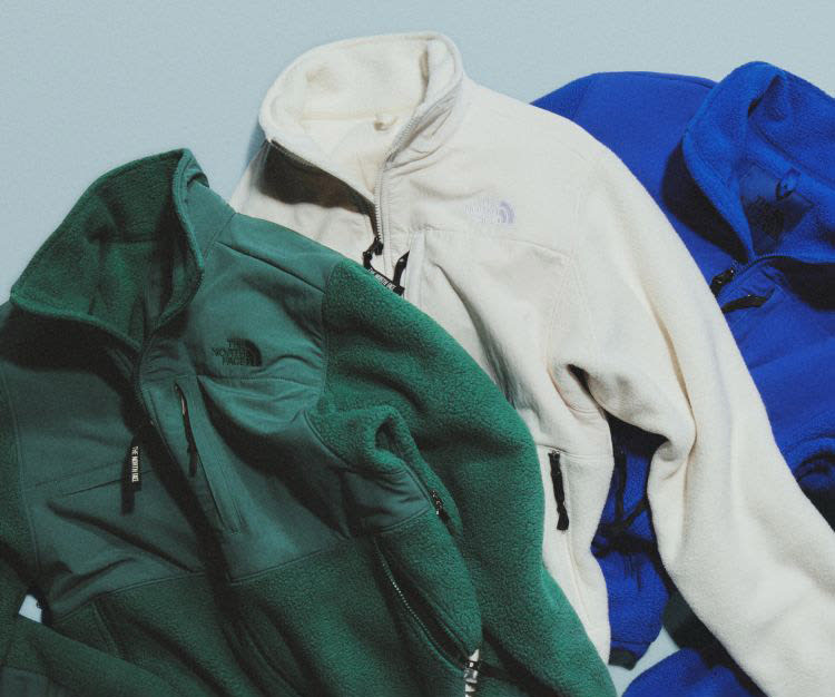 Jacket made by The North Face in Evergreen, White Dune, and TNF Blue laying on a gray background