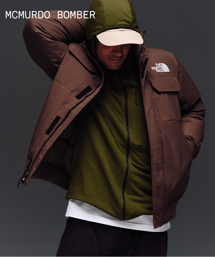 Male model reaching his hand behind his head in McMurdo Bomber in Smokey Brown over a green hoodie.