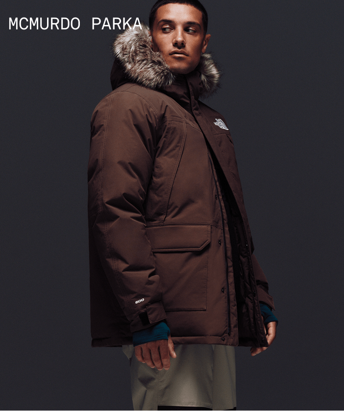 Male model looking stoic, wearing McMurdo Parka in Smokey Brown with fur-trimmed hood.